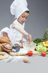 Caucasian Girl In Cook Uniform Making Food in Kitchen Glassware with Whisk In Studio Environment.Posing Against Gray Background.