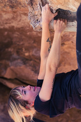 Naklejka premium Thin blonde caucasian woman with arm tattoos hangs upside down while she rock climbs on boulders in the desert of California
