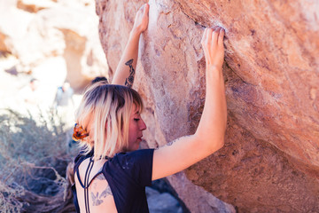 Thin blonde caucasian woman with arm tattoos rock climbs on boulders in the desert of California
