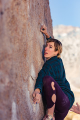 Thin blonde caucasian woman wearing flannel against the cold rock climbing on boulders in the desert of California