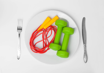 jumping rope with dumbbells in food dish with fork and knife, healthy lifestyle concept