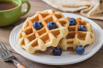 Waffle with blueberry on plate and cup of tea