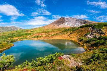Fototapeta na wymiar 北海道の大雪山・旭岳に広がる色とりどりの紅葉と青空・鏡貼りの池