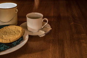 Evening  steamy tea and sugar cookie on a green napkin and white plate, wooden table with candle