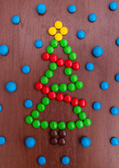 Christmas green pine tree made of colorful sweet chocolate round candies New year 2018 on a rustic wooden background . Holiday concept. Snow imitation and Garland