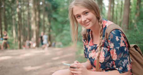 Young woman using a smartphone in a forest. Beautiful caucasian girl typing on phone in the woods. 