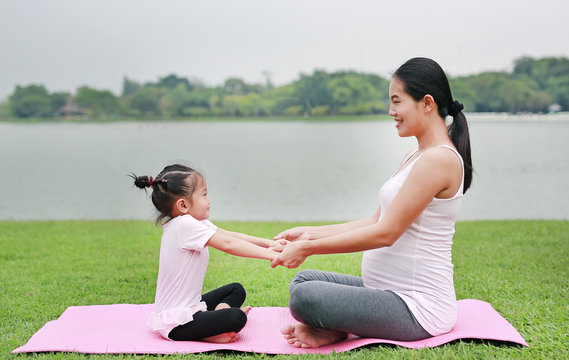 Pregnant woman and her child girl doing yoga in the public park.