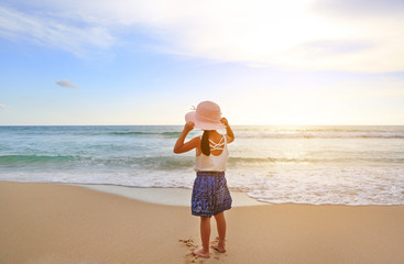 Rear view little girl wear straw hat standing at the beach.