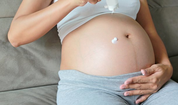 Pregnant Woman applying stretch marks cream on her belly.