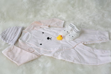 Collection items of bodysuits for newborn babies with socks on white fur background.