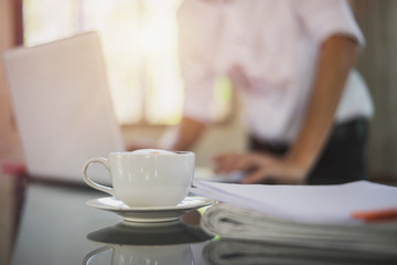 A white cup of coffee on glass table and businessman working blur background