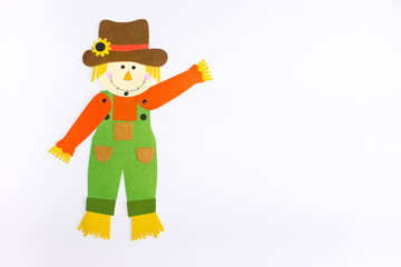 Waving Felt Scarecrow decoration photographed against a white background.  He is wearing green overalls, an orange shirt and a brown hat adorned with a sunflower. 