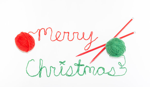 Merry Christmas Written in red and green Yarn with Crossed red Knitting Needles. Photographed against a white background. 