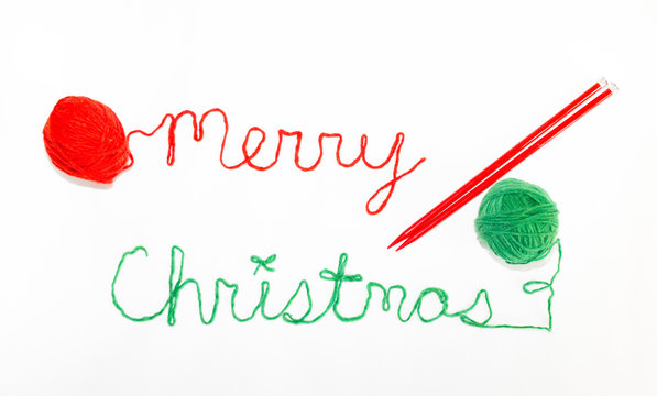 Merry Christmas Written in red and green yarn with red knitting Needles in Parallel. Photographed against a white background,.