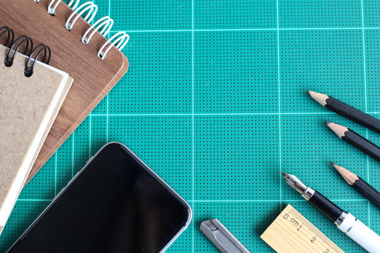 Flat lay book, smart phone, ruler and pencils on green desk