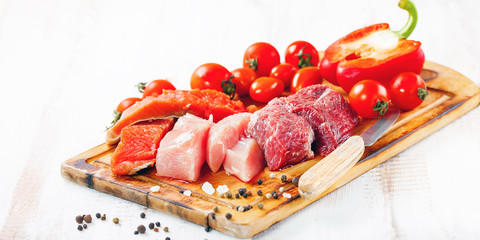 Products for a diet - raw meat of beef and chicken, a salmon and vegetables on a light wooden background. Selective focus.