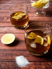 Glasses of cocktail with ice and lemon on wooden table close-up
