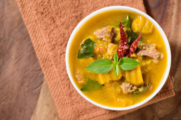 Thai food.Spicy pumpkin soup with pork in a bowl on brown fabric and wooden background.Top view of food