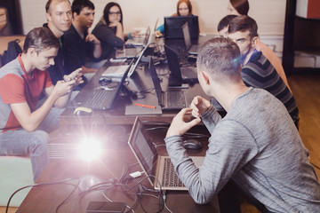 Group of people working in a team by computers sitting at a table lighting a projector ray