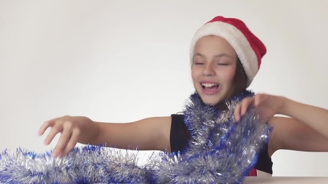 Beautiful teen girl in Santa Claus hat and New Year's tinsel happily and mischievously dances on white background stock footage video