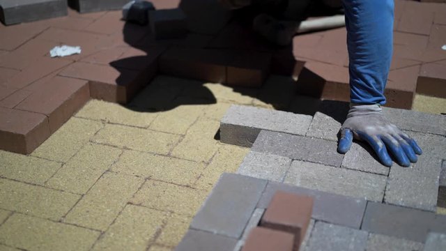 Closeup of man fitting bricks into a hardscaping custom design in herringbone pattern.