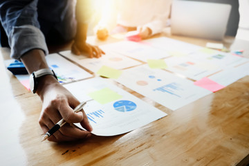 Businessmen holding pens and holding graph paper are meeting to plan sales to meet targets set in...
