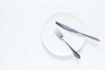 Empty white ceramic plate, knife and fork on a white background