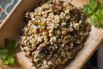 Traditional lentils salad with dried tomatoes, olives and couscous in a wooden plate with fresh parsley for garnish