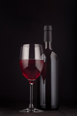 Bottle of red wine and wine glass mock up on elegant dark black wooden background, vertical. Template for portfolio, advertising, design, branding identity, cover magazine, bar and restaurant menu.
