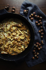 Apple pie on a baking sheet against a linen napkin with hazelnuts on a wooden table in rustic style. Flat lay