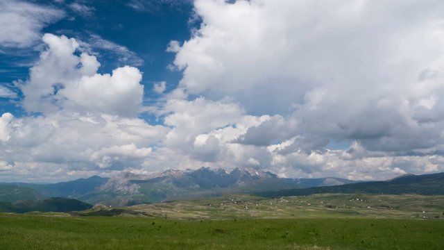 Clouds over the green meadow with majestic mountains in the background