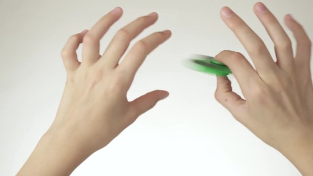 Hands of a teenage girl spin a green fidget spinner on white background stock footage video