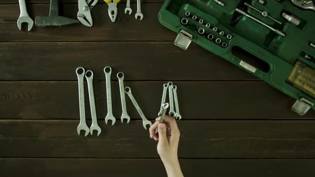 A man sits at a table near the tools are and lays out the spanners in size and folds back and count them.