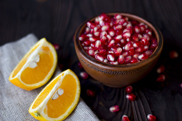 ruby pomegranate seeds on the plate and slices of orange on a wooden table