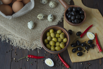 quail and chicken eggs, olives, chili and spices on a wooden table