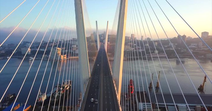 Ascending above the road between stay cables of Zolotoy Bridge (Golden Bridge, cable-stayed bridge across Zolotoy Rog harbour built in 2012). Aerial view of cars driving across it. Vladivostok, Russia