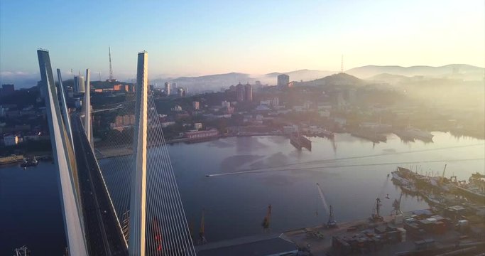 Aerial view of the Golden Bridge (cable-stayed bridge built in 2012) across the Golden Horn harbour. Motorboat flows under it. Morning Vladivostok city is on the background. Russia. Autumn