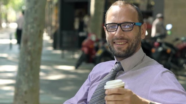 Portrait of happy businessman drinking coffee on bench in city 
