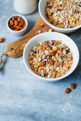High angle view of the breakfast for two person with muesli with almond nuts and dried berries in white bowls and the bottle of milk on the blue textured table.