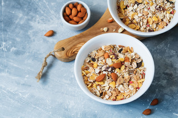 High angle view of the breakfast for two person with muesli with almond nuts and dried berries in white bowls on the blue textured table.