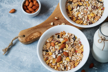 High angle view of the breakfast for two person with muesli with almond nuts and dried berries in white bowls and the bottle of milk on the blue textured table.