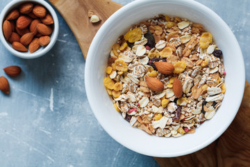 Top view of the white bowl with muesli with almond nuts and dried berries in  on the blue textured table. Copy space.