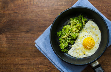 Fried egg with broccoli and cheese in a iron frying pan on the brown wooden table background. with copy space. top view