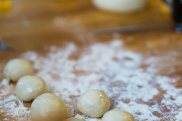 Fototapeta na wymiar Closeup of small balls ready dough on floured kitchen table. Defokus in the background.