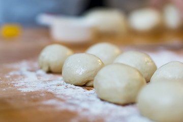 Fototapeta na wymiar Closeup of small balls ready dough on floured kitchen table. Defokus in the background.