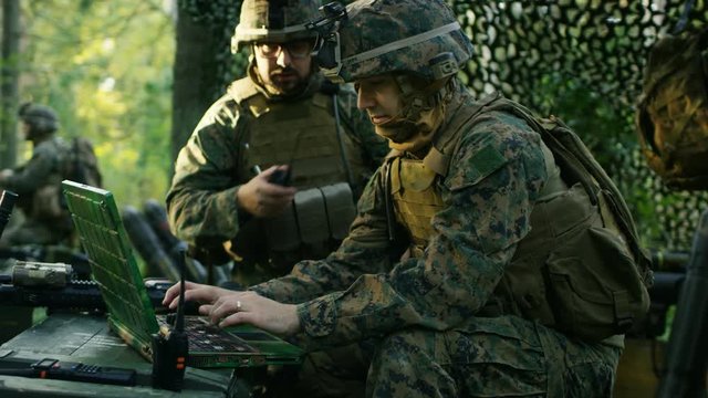 Military Staging Base, Officer Gives Orders to Chief Engineer, They Use Radio and Army Grade Laptop. They're in Camouflaged Tent in a Forest. They're on Reconnaissance Operation/ Mission.