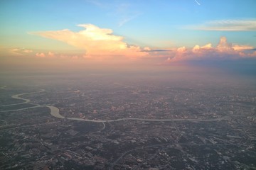 Fototapeta premium Aerial view of Bangkok, Thailand, with building in big city, evening sky and colorful cloud. View from airplane's window. Soft focus with low key.
