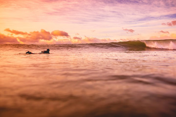 Fototapeta na wymiar Wave in ocean at bright sunset or sunrise with surfer. Wave with warm sunrise colors
