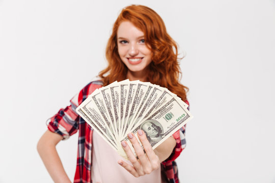 Cheerful pretty young redhead lady holding money.