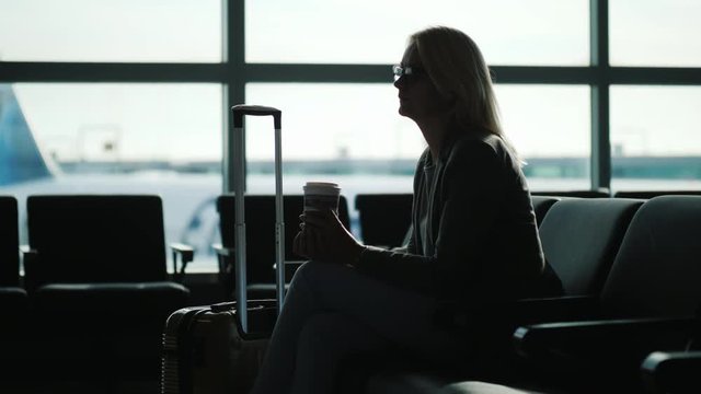 A Business Woman Is Drinking Coffee From A Paper Cup At The Airport Terminal. Passenger Waiting For The Flight